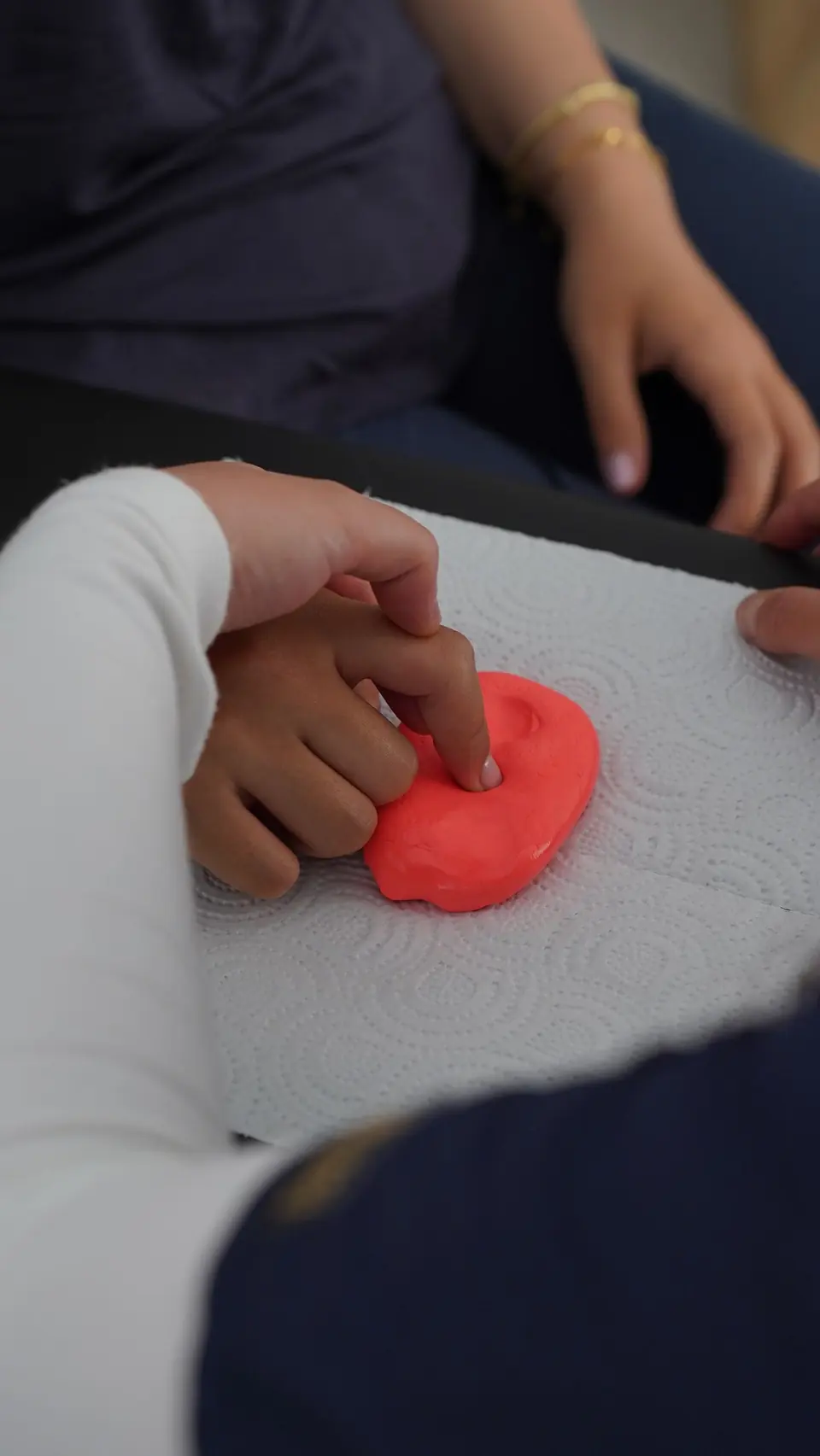 Manos de una niña trabajando la motricidad con plastilina junto a una adulta